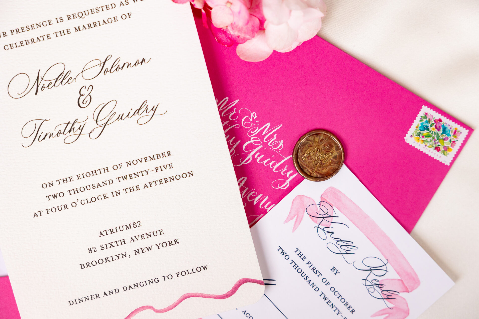 Wedding invitation suite with a fuchsia envelope addressed in white calligraphy, a gold wax seal, and a floral stamp