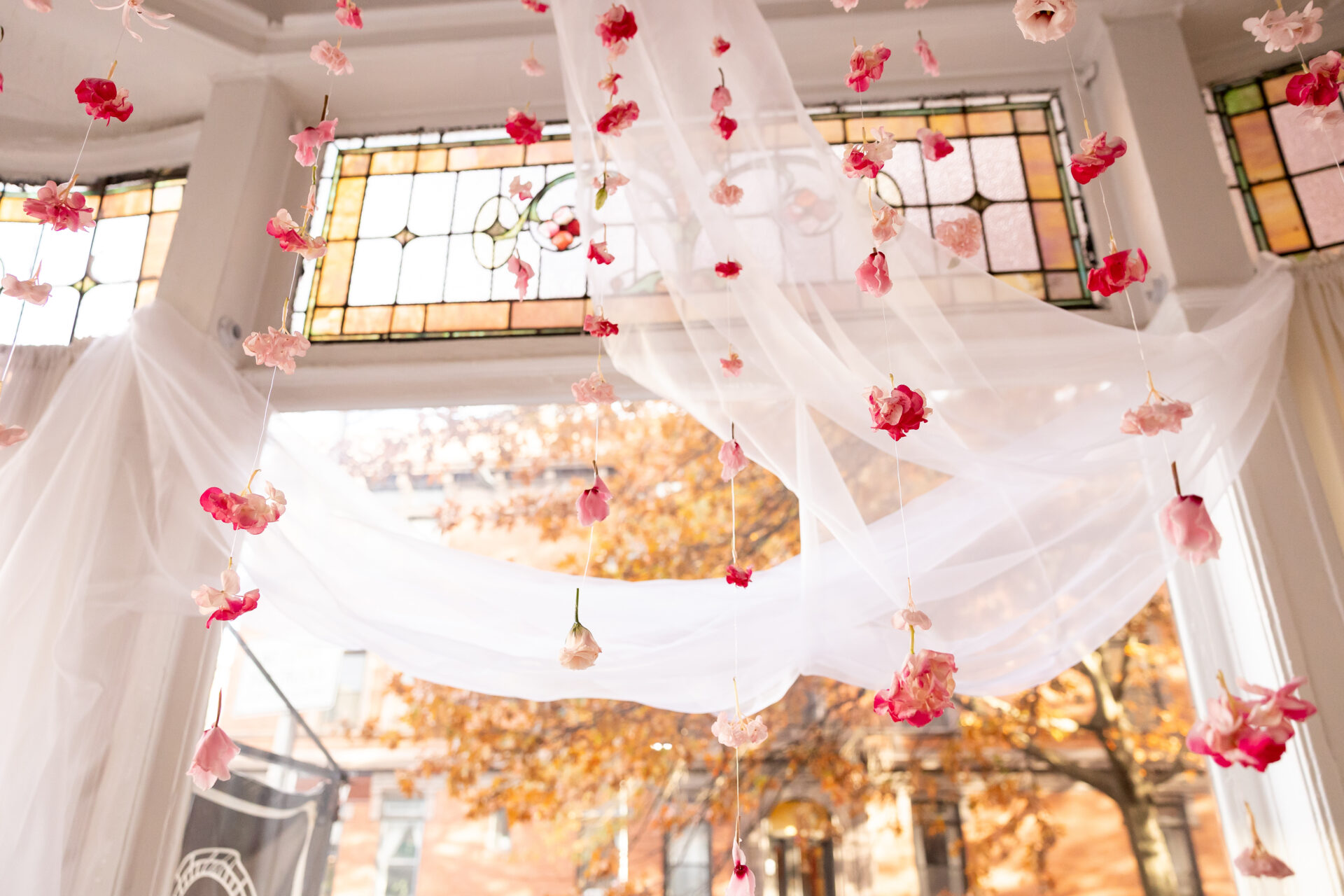 Hanging flower ceremony backdrop for a Brooklyn brownstone elopement, with pink blooms strung under white chiffon and stained-glass transoms