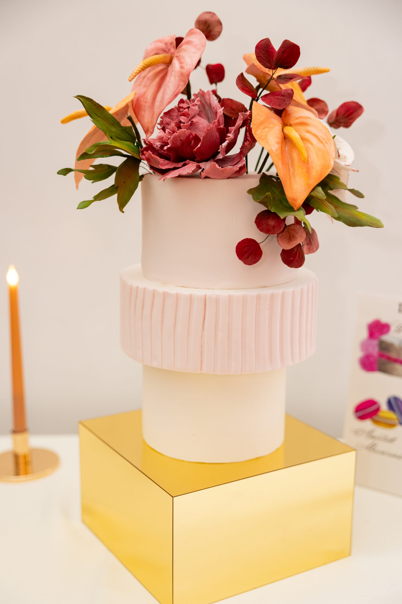 Modern pink wedding cake with a wider pleated middle tier, topped with sugar anthurium and a sugar peony