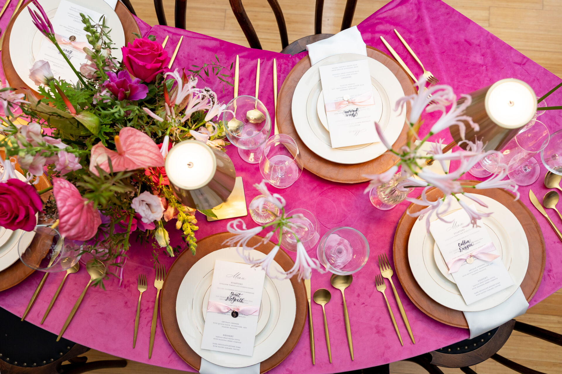 Overhead view of a fuchsia velvet wedding tablescape with cognac leather chargers, gold flatware, and calligraphed menus tied with blush ribbon