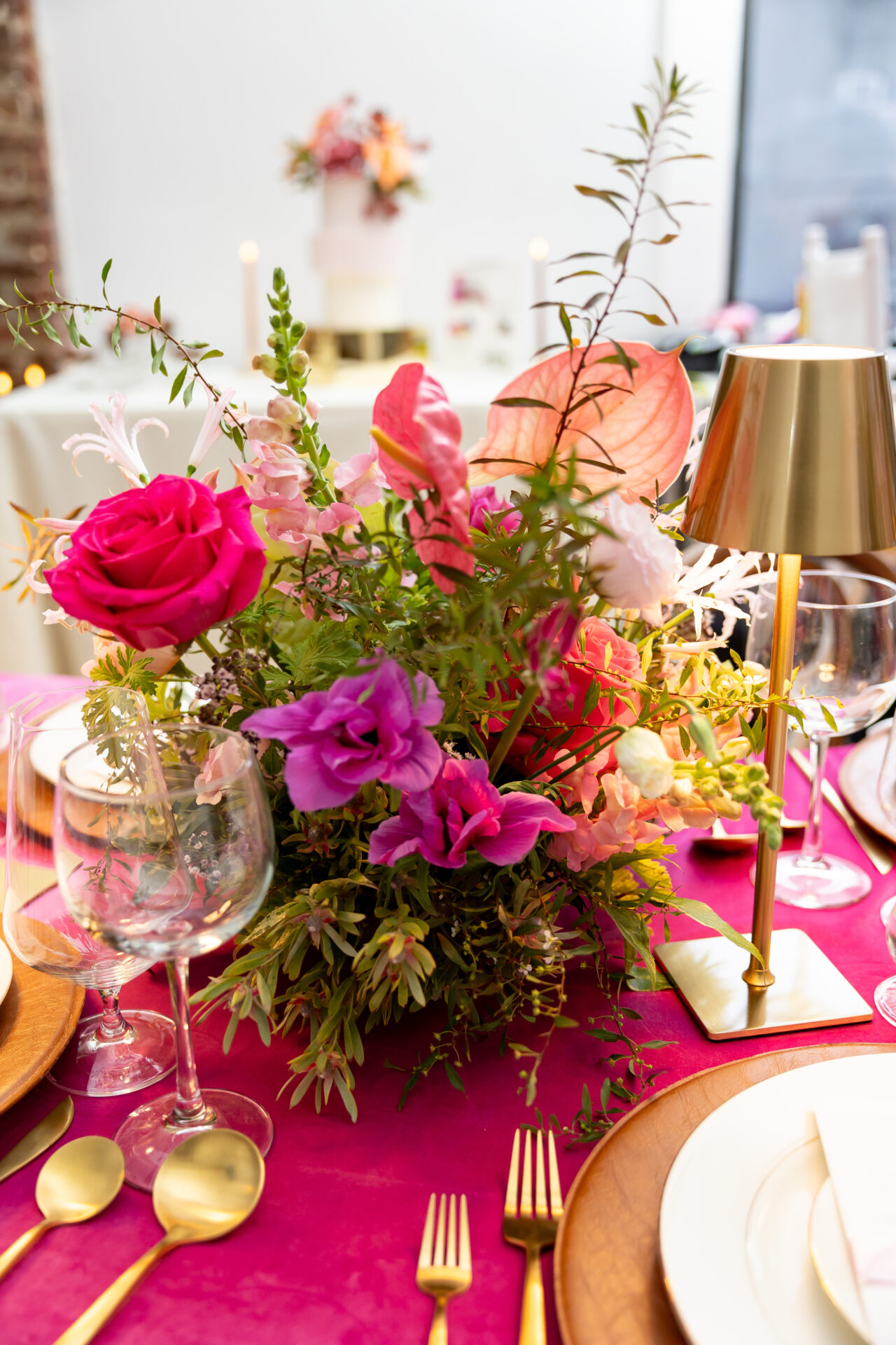 Wedding centerpiece of hot pink roses, blush anthurium, and snapdragons beside a gold cordless lamp on fuchsia velvet