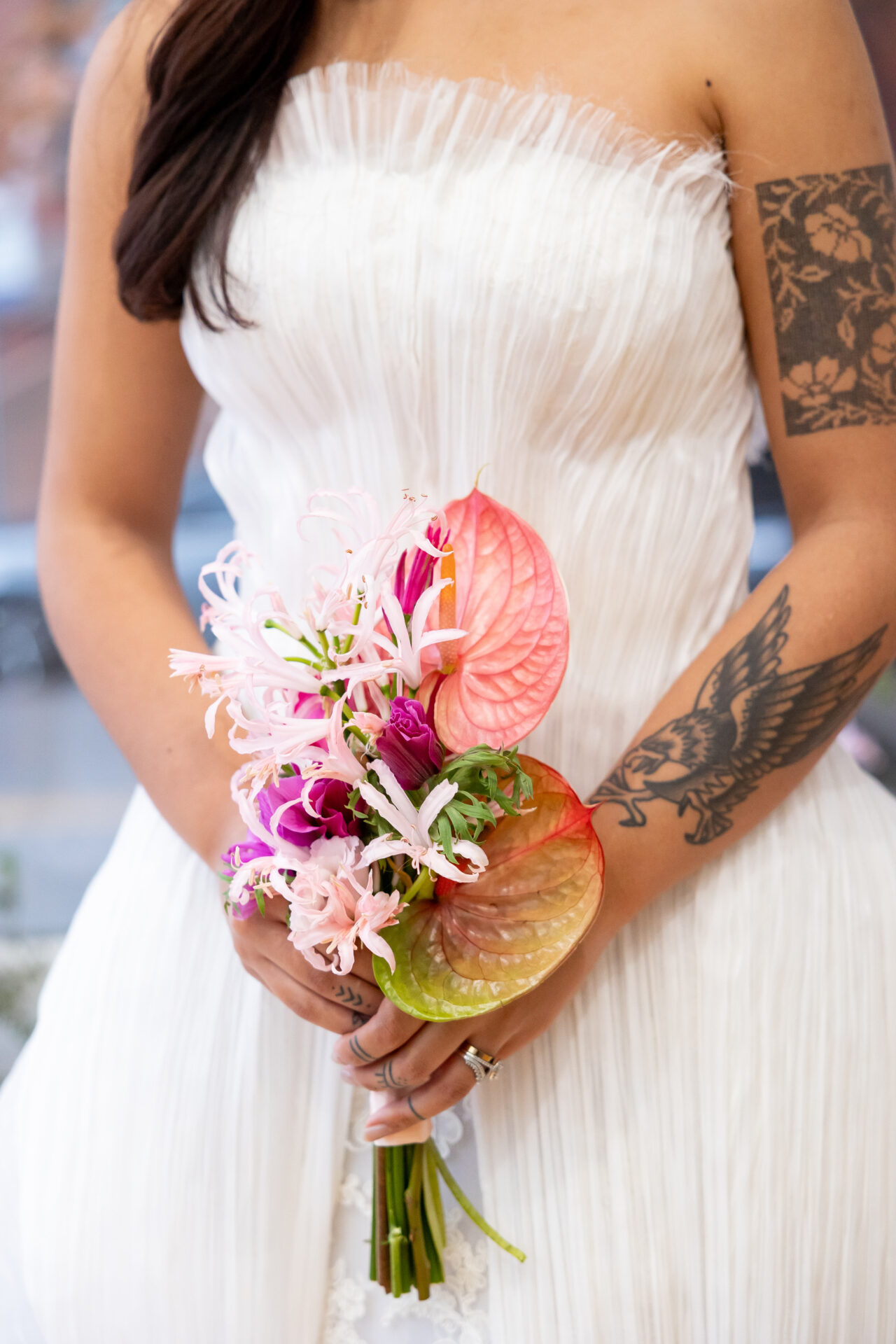 Anthurium wedding bouquet with coral and pink-to-green anthurium, pale pink nerines, and a magenta anemone held against a pleated white bodice