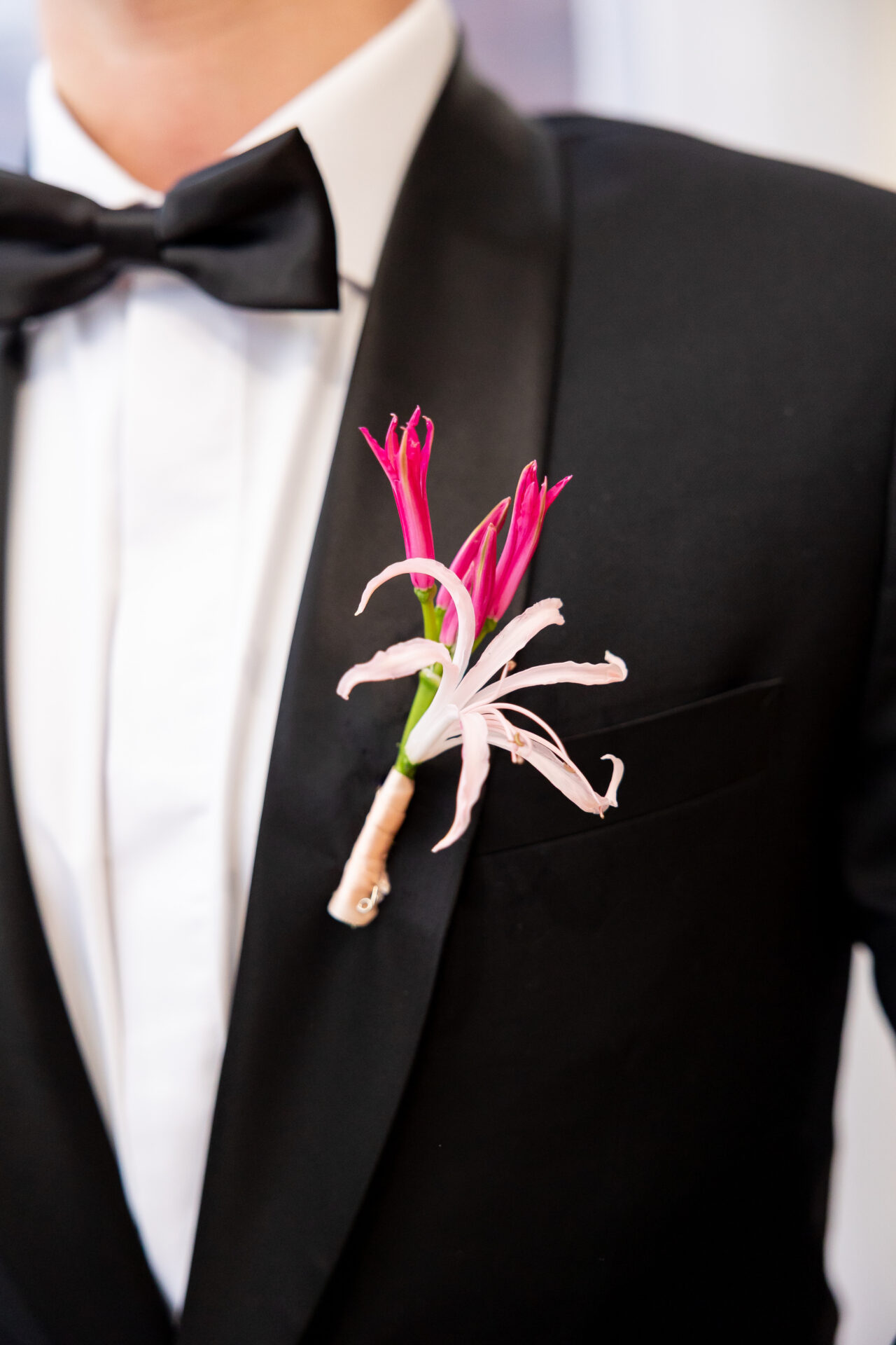Pink and fuchsia nerine boutonniere wrapped in blush ribbon on a black shawl-collar tuxedo